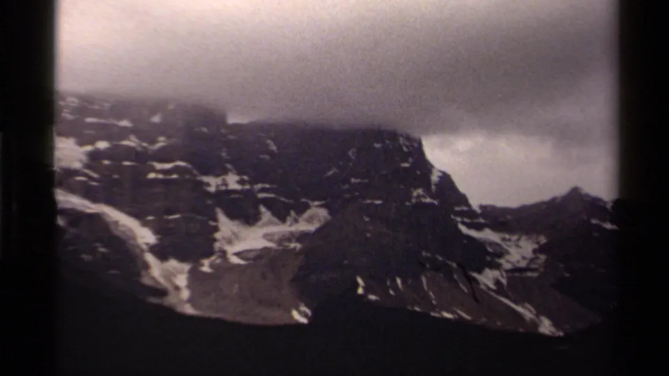 1979 Canadian 8mm frame of a shadowed mountain ridge, snow streaks, and low cloud softening the summit line.