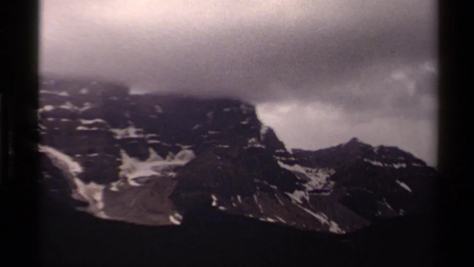 1979 Canadian 8mm frame showing snow-dusted slopes and a dark ridge beneath thick stormlike cloud cover.