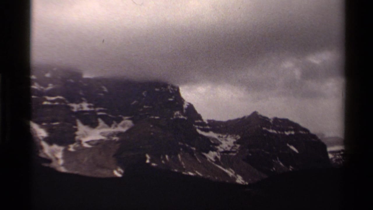 Dark rocky mountain ridge with snow patches under a heavy cloudy sky.