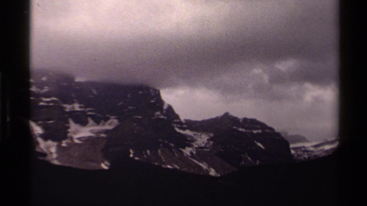 1979 8mm Canada view of rugged snow-patched mountains under a thick gray cloud bank.