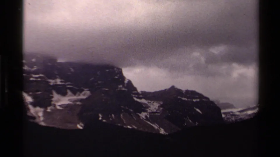 1979 8mm Canada view of rugged snow-patched mountains under a thick gray cloud bank.