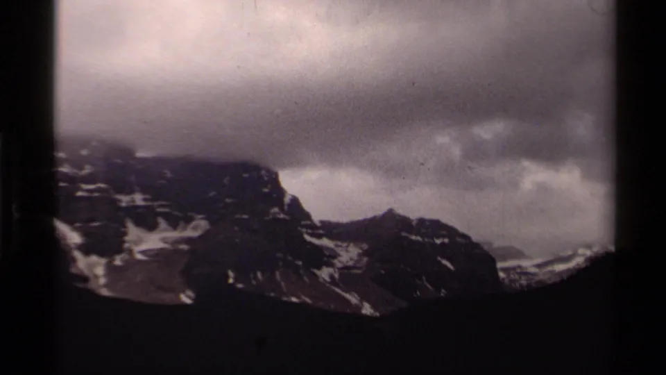 1979 8mm Canada mountain landscape with patchy snow, low clouds, and a dark silhouetted foreground slope.