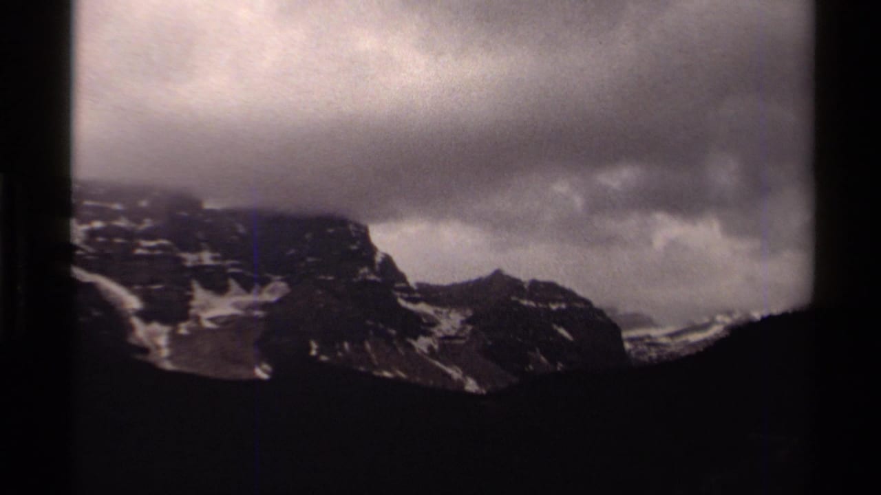 1979 Canada 8mm view of a distant snowy mountain ridge under heavy cloud cover, framed by dark film edges.