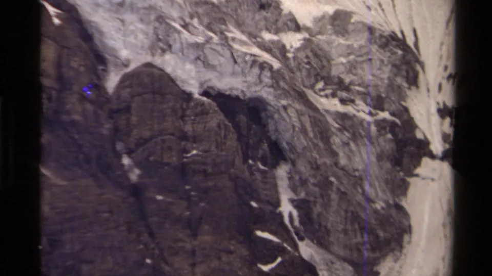 Closer 8mm view of a rugged Canadian mountain face, showing dark rock, pale snowfields, and handheld film texture.