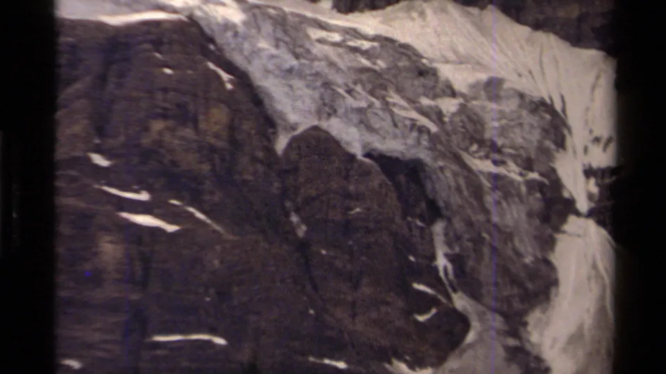 Close 1979 8mm mountain view in Canada, with a dark rocky cliff beside a pale snowfield and soft archival grain.