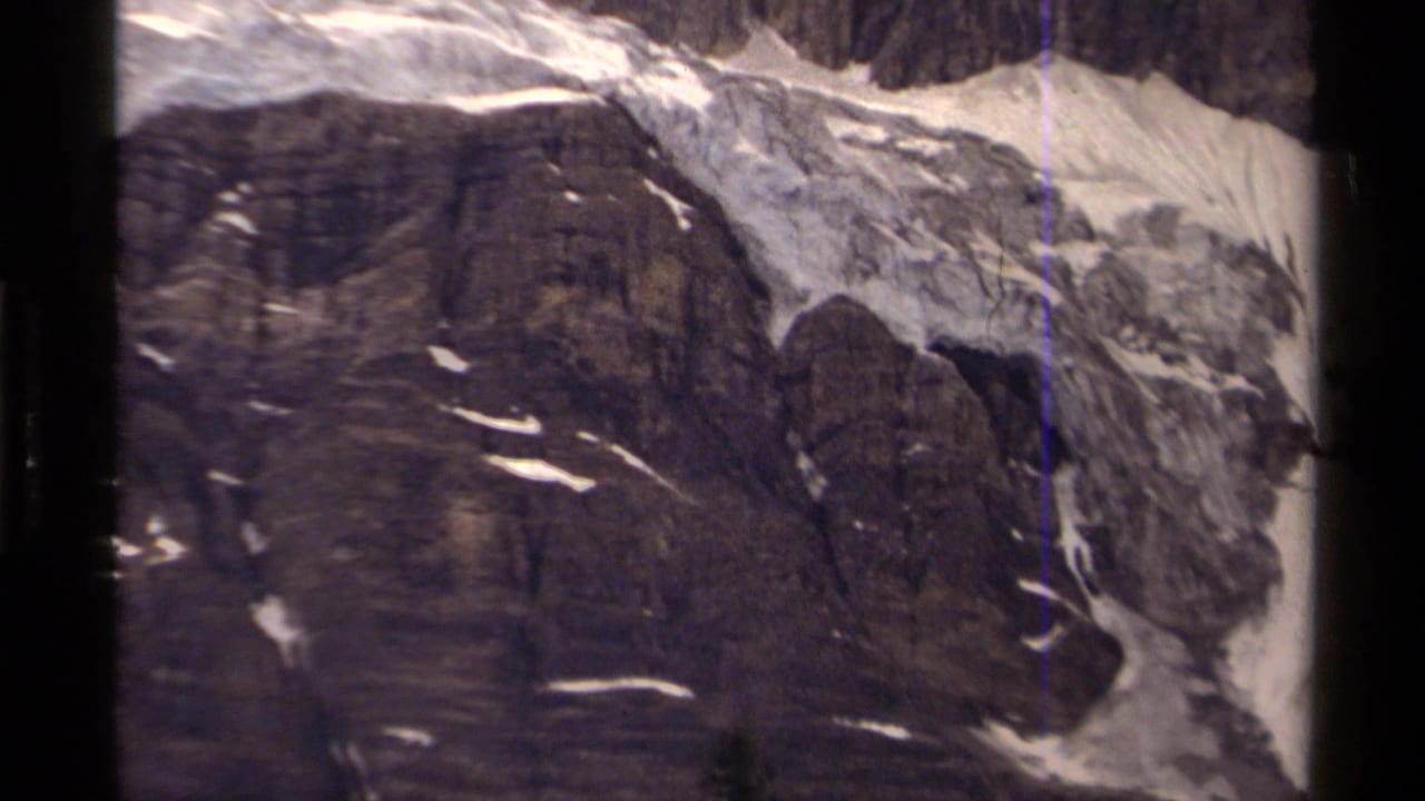 Snow-dusted rocky mountain face framed by black 8mm film borders.
