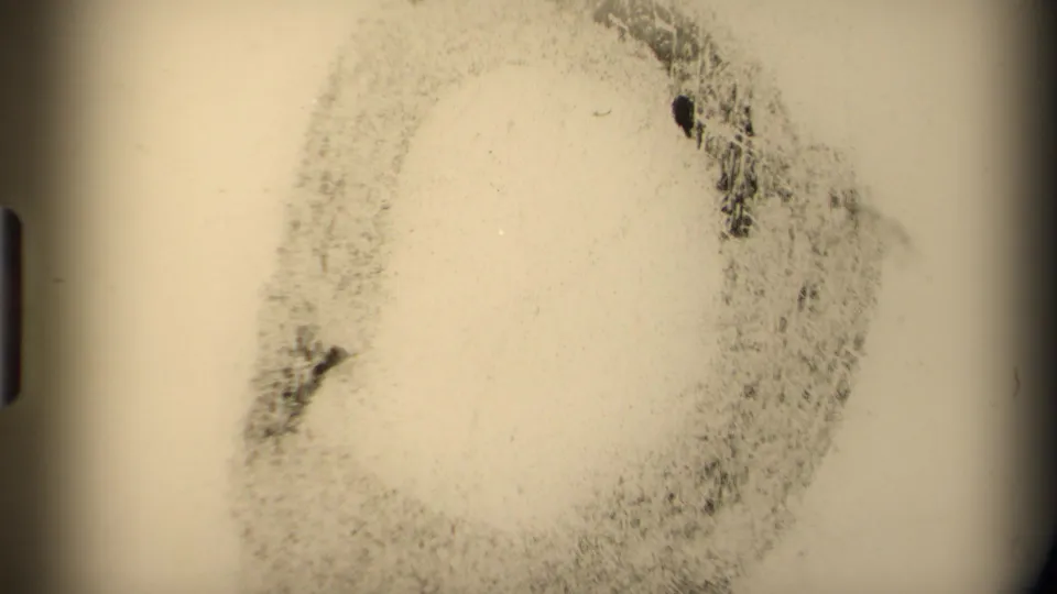 Pale 8mm frame with mottled grain, a circular dark mark, and rounded black frame edges, likely a film artifact or transitional exposure.