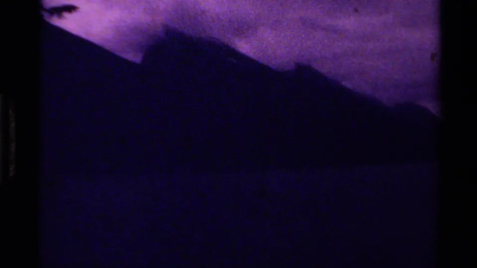 1979 Canadian 8mm frame with a dark mountain silhouette below a purple-toned sky and heavy film grain.