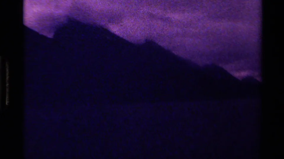A dark mountain ridge sits below a purple, clouded sky in 1979 Canadian 8mm home-movie footage.
