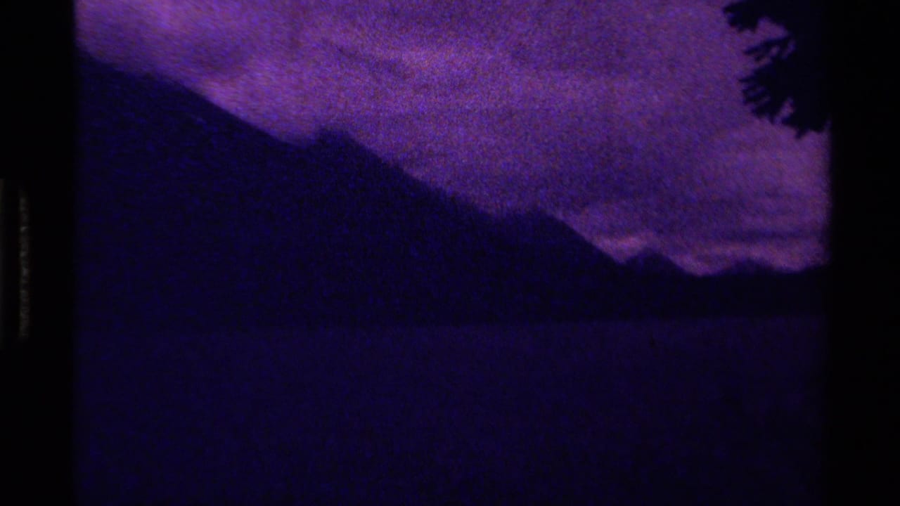 1979 Canadian 8mm frame with a silhouetted mountain ridge, purple sky, dark water, and a tree edge.