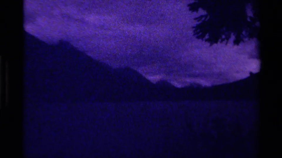 1979 Canadian 8mm frame of a purple-blue sky, dark mountain form, water surface, and branch silhouette.