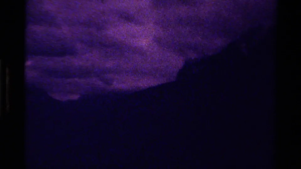 1979 Canada 8mm frame with dense grain, purple clouds, a dark mountain slope, and very low-light blue foreground terrain.