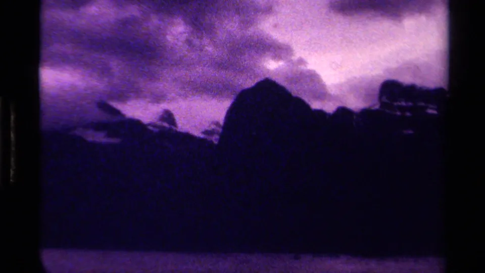 1979 Canadian 8mm frame showing jagged silhouetted peaks, tree shapes, and brighter cloud breaks.