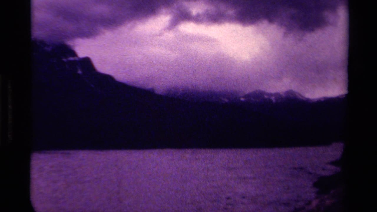 1979 Canadian 8mm frame showing a purple-tinted lake, distant dark mountains, and heavy cloud cover.