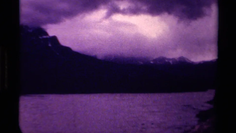 1979 Canadian 8mm frame showing a purple-tinted lake, distant dark mountains, and heavy cloud cover.
