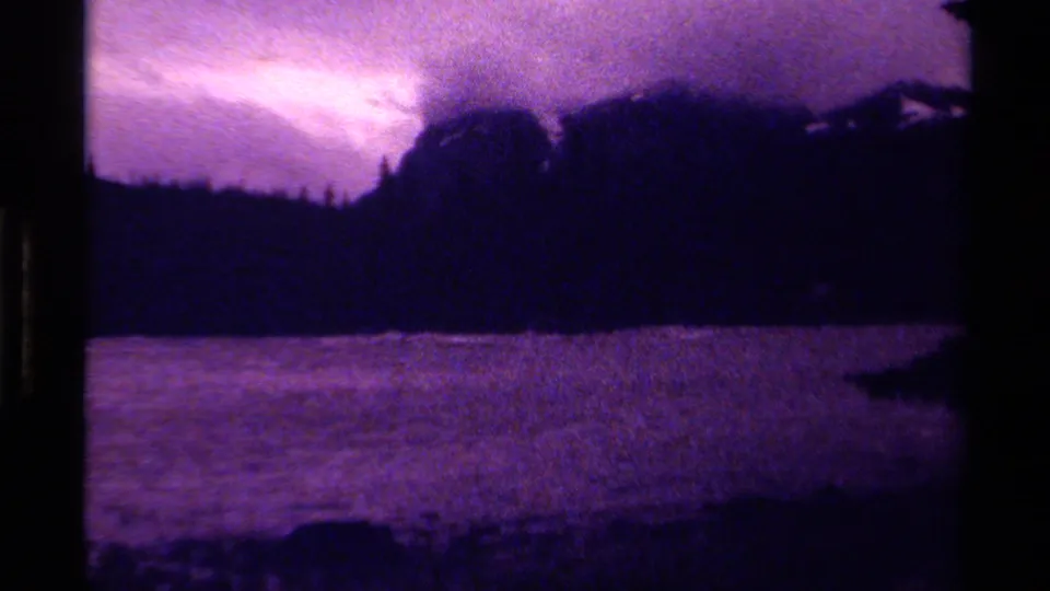 Canadian 8mm landscape frame with rippled water, forested shore, dark mountain forms, and a bright purple cloud opening.