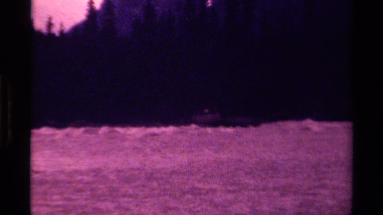 1979 Canada 8mm frame showing choppy purple water beneath a dark tree-lined shore and dim sky.