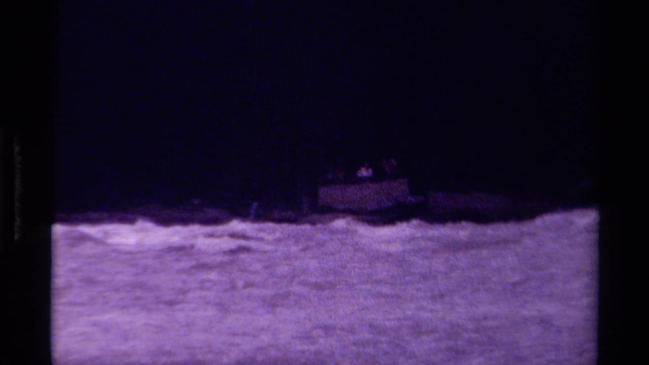 Small boat rides on choppy water near a dark shoreline.