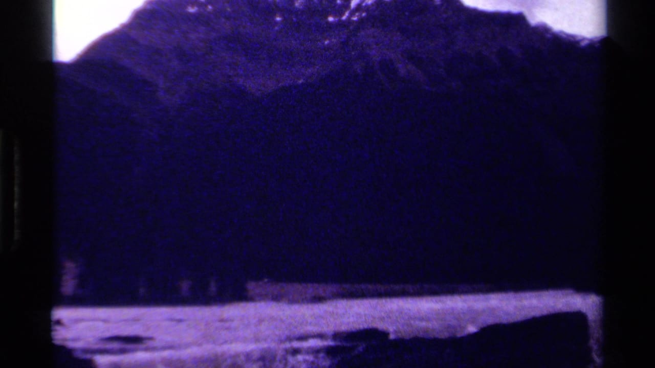 1979 Canada 8mm frame showing a dark mountain slope beyond a rushing river with rocks in the foreground.