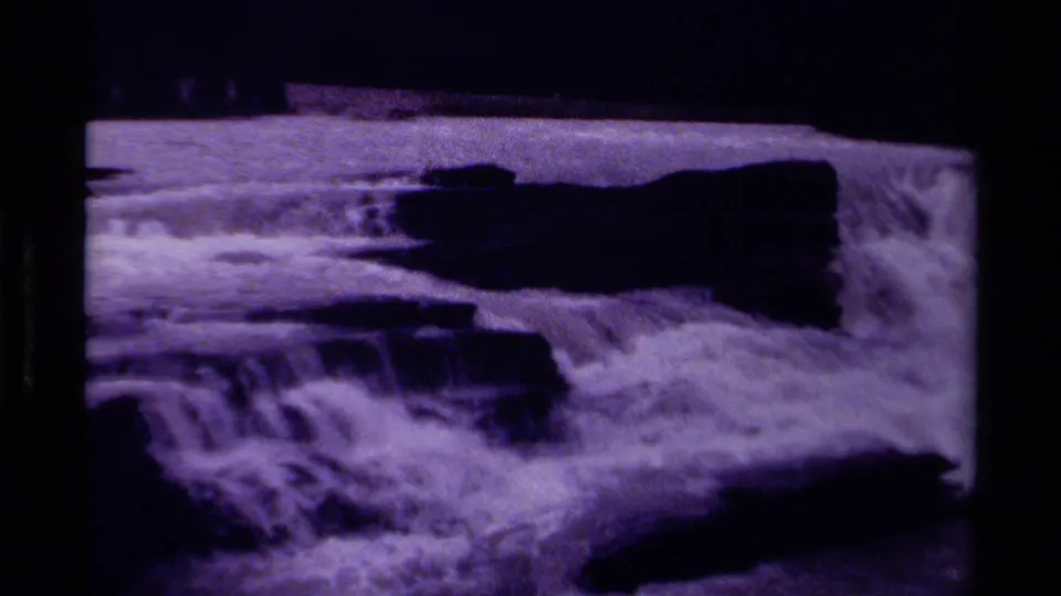 1979 Canada 8mm landscape frame with broad foaming whitewater, rocks, and dark wooded hills in the distance.