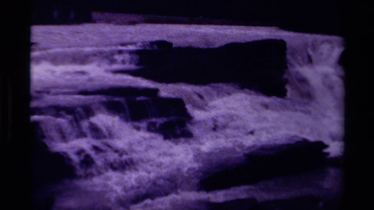 1979 Canada 8mm home-movie frame showing a waterfall rushing across dark rock ledges with purple color fading and grain.