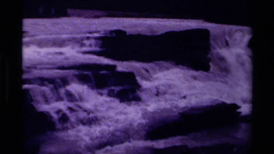 1979 Canada 8mm home-movie frame showing a waterfall rushing across dark rock ledges with purple color fading and grain.