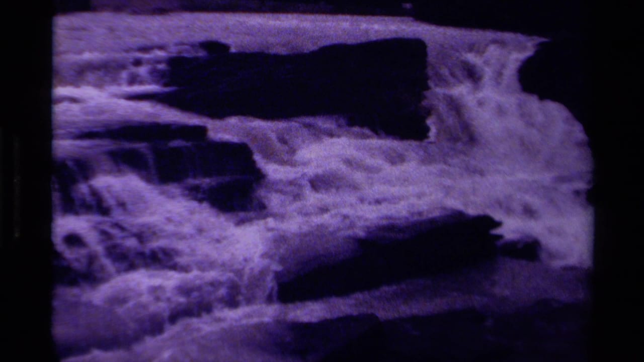 Waterfall foam spreads across dark rock ledges in a grainy purple frame.