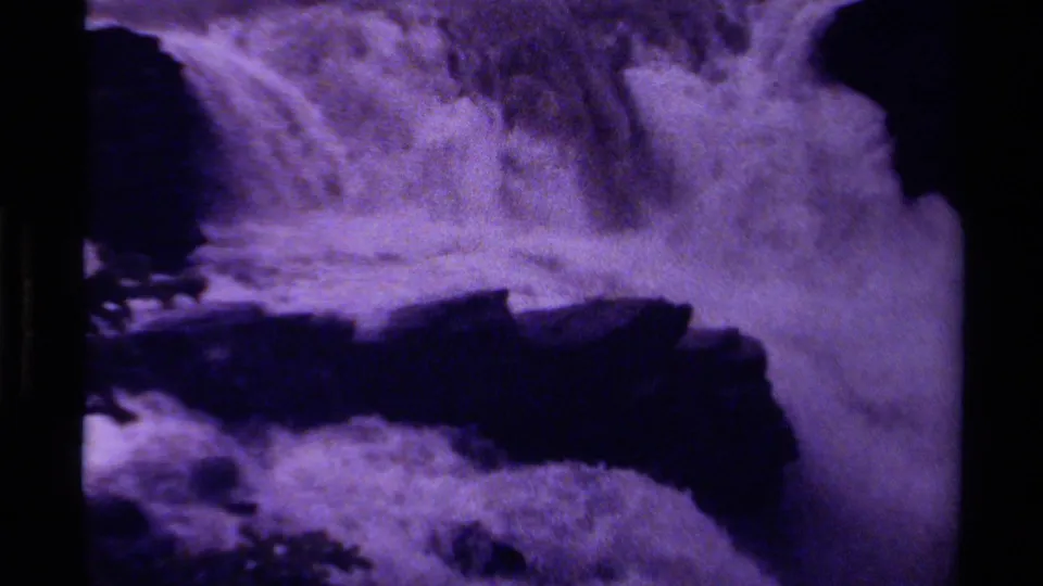 1979 Canada 8mm frame showing dense waterfall foam and spray against dark rock, with strong purple-tinted grain.