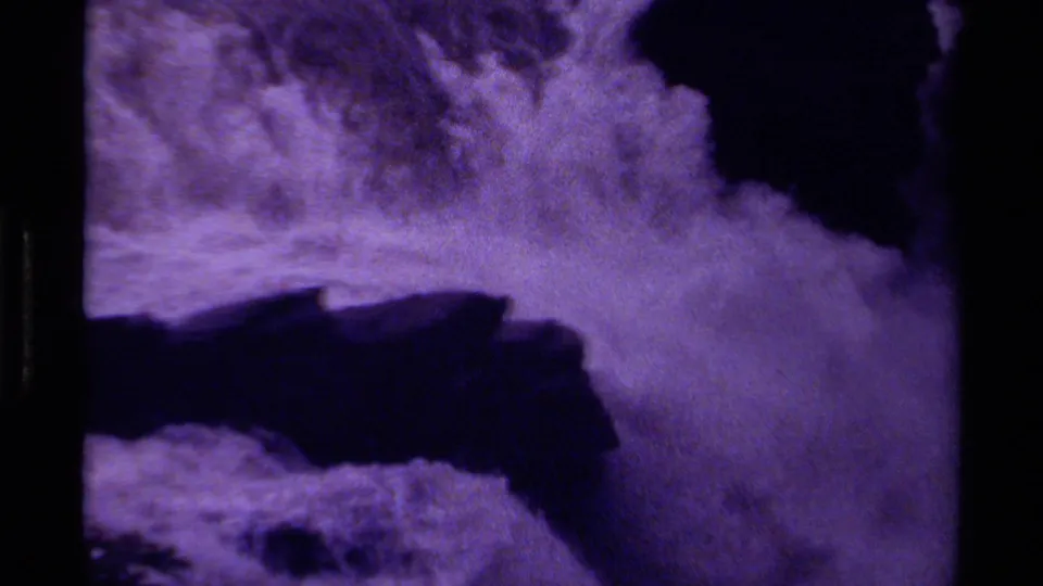 1979 Canada 8mm frame of a broad white waterfall plume crashing past dark rock with soft grain and purple cast.