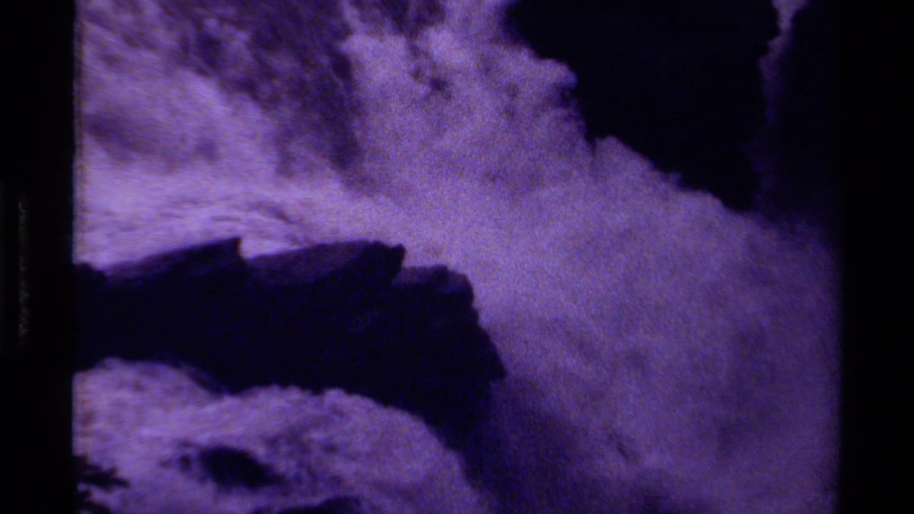 Purple-tinted waterfall rushing over dark rock ledges with black film borders.