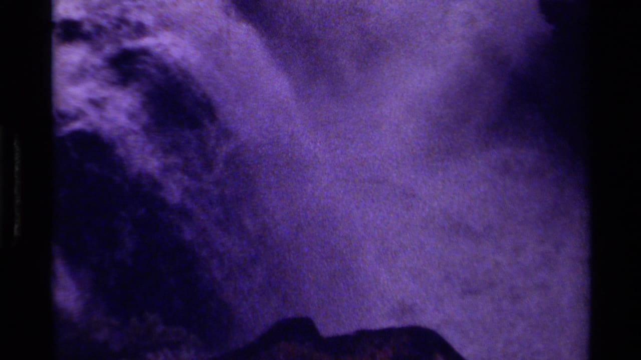 Purple-tinted view of a waterfall channel framed by dark rock and film borders.