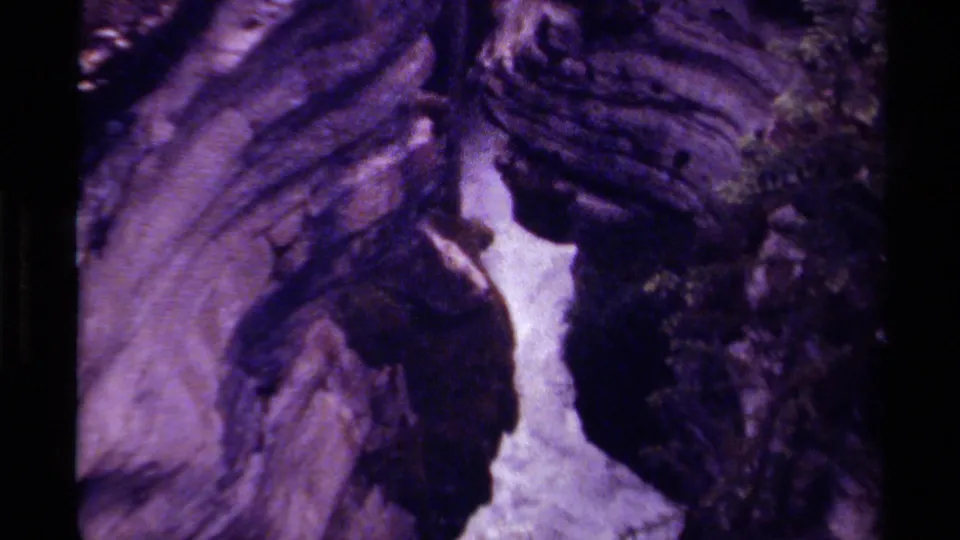 Purple-tinted 8mm frame showing a Canadian waterfall channel flowing through shadowed rock walls.