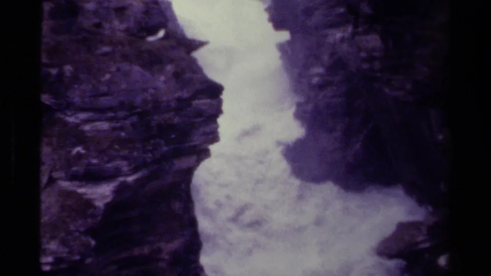 Canadian 8mm home-movie frame of turbulent water filling a narrow gorge, bordered by rugged dark stone.