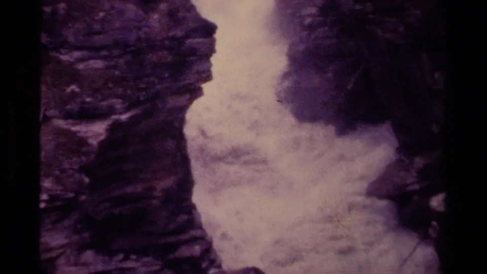 1979 8mm frame from Canada showing a lower view of churning waterfall water beneath steep purple-toned rock.