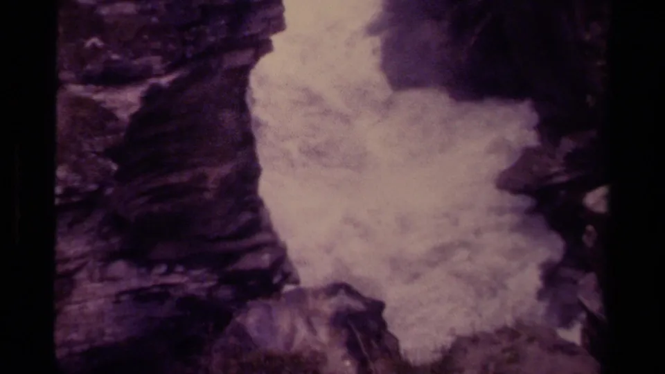 Vintage Canadian 8mm frame showing foaming waterfall water compressed between dark gorge walls and shadowed rock.