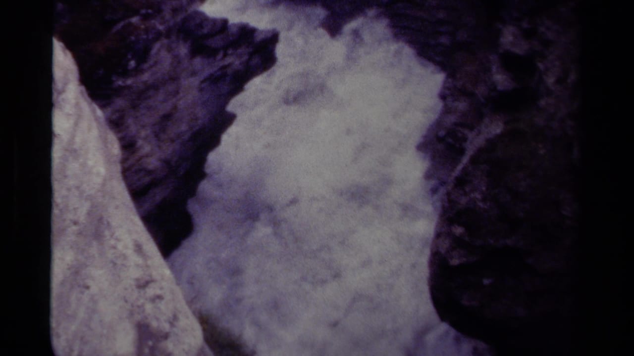 Foaming water beside a pale rock face and dark cliff edges.