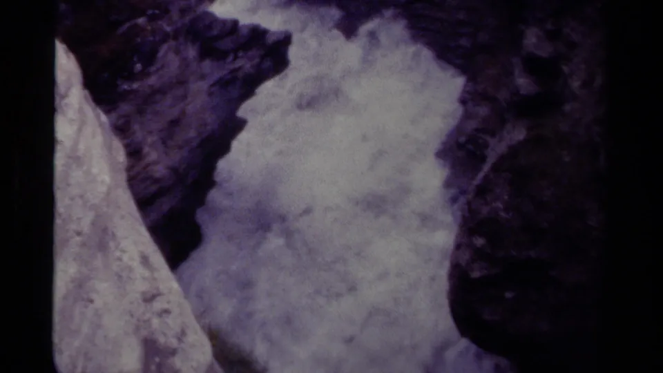 1979 Canadian 8mm frame with white water churning beside a pale rock face in a dark rocky gorge.