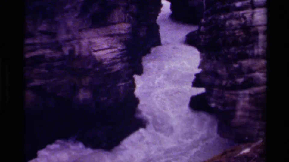 Vintage 8mm Canada frame showing a bright waterfall channel bordered by rugged, shadowed canyon rock.