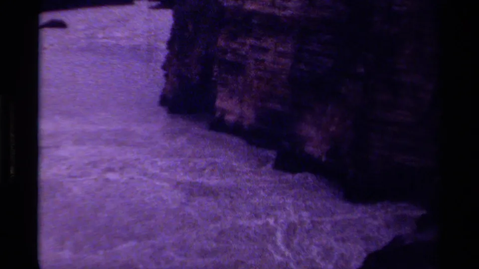 1979 Canada 8mm frame showing pale rushing water below a rugged, shadowed rock wall in a mountain canyon setting.