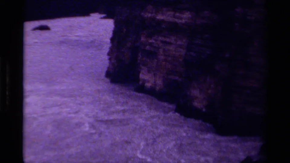 1979 Canada 8mm frame of white water passing a steep, shadowed rock wall, with visible grain and purple color shift.