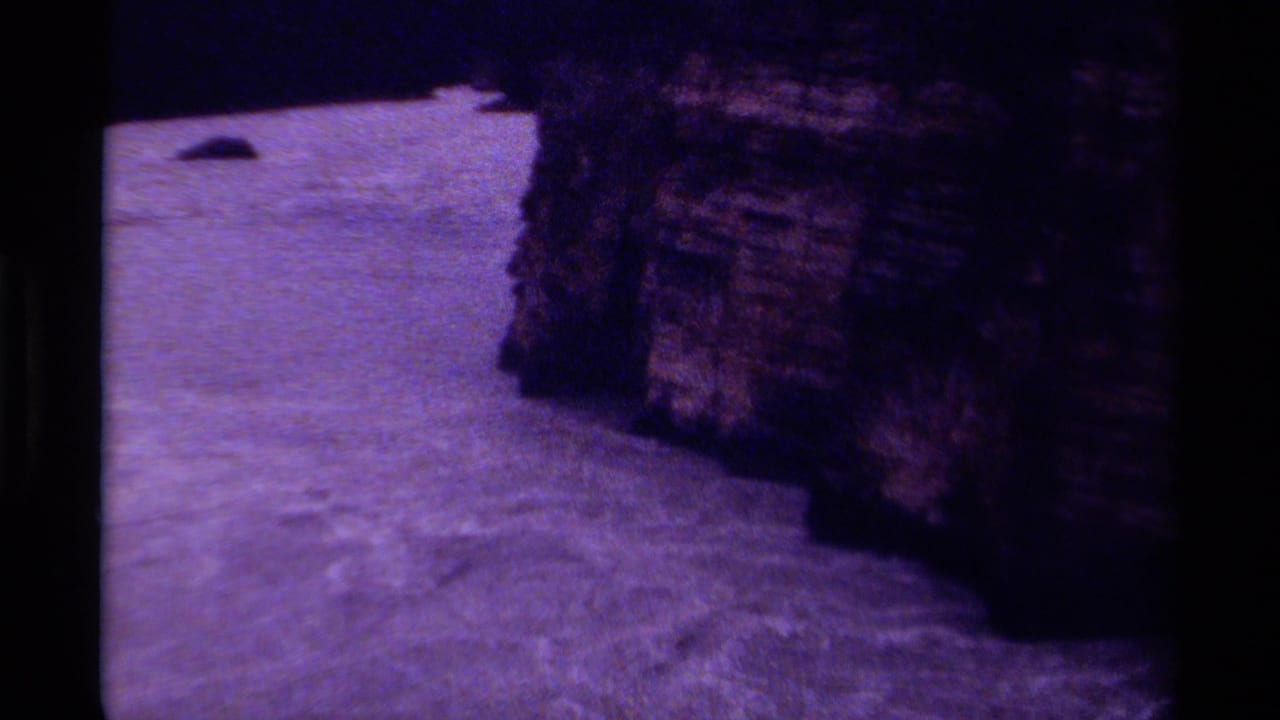 1979 Canadian 8mm frame showing rippled river water bending around a shadowed rocky edge with heavy grain and purple color shift.