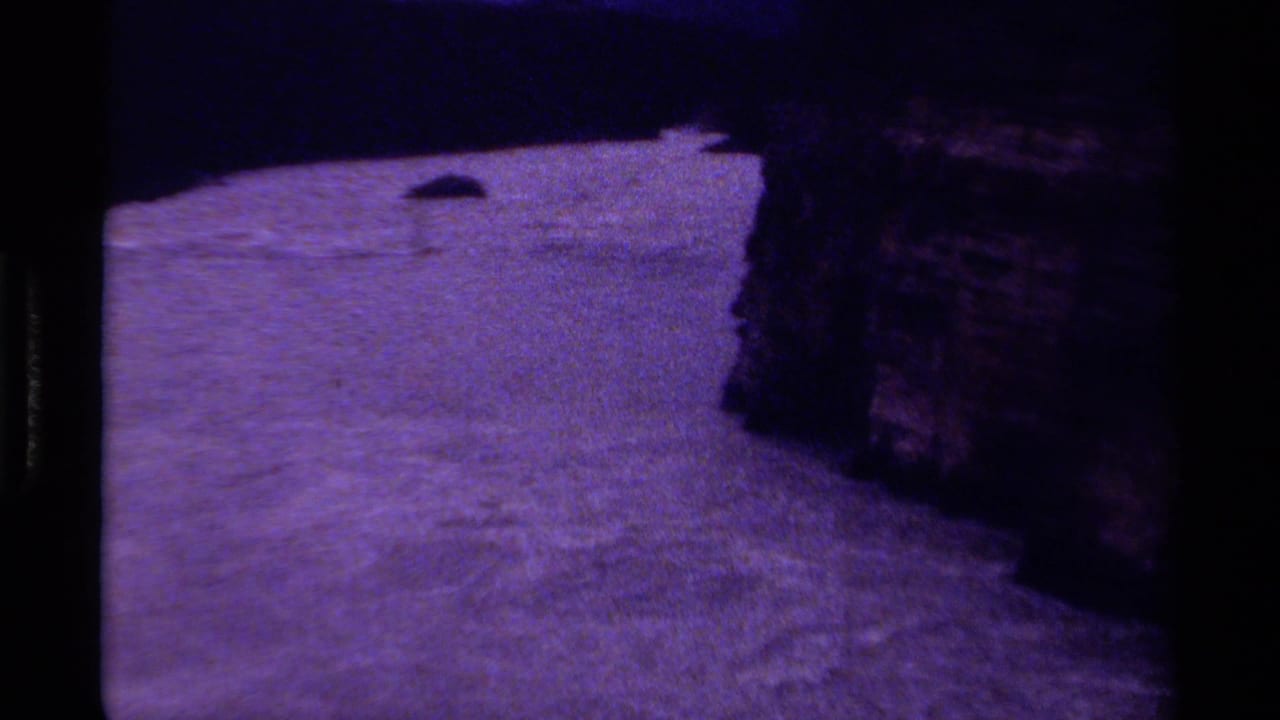 1979 Canadian 8mm frame of textured river water near a shadowed cliff face, with a small dark object visible on the surface.
