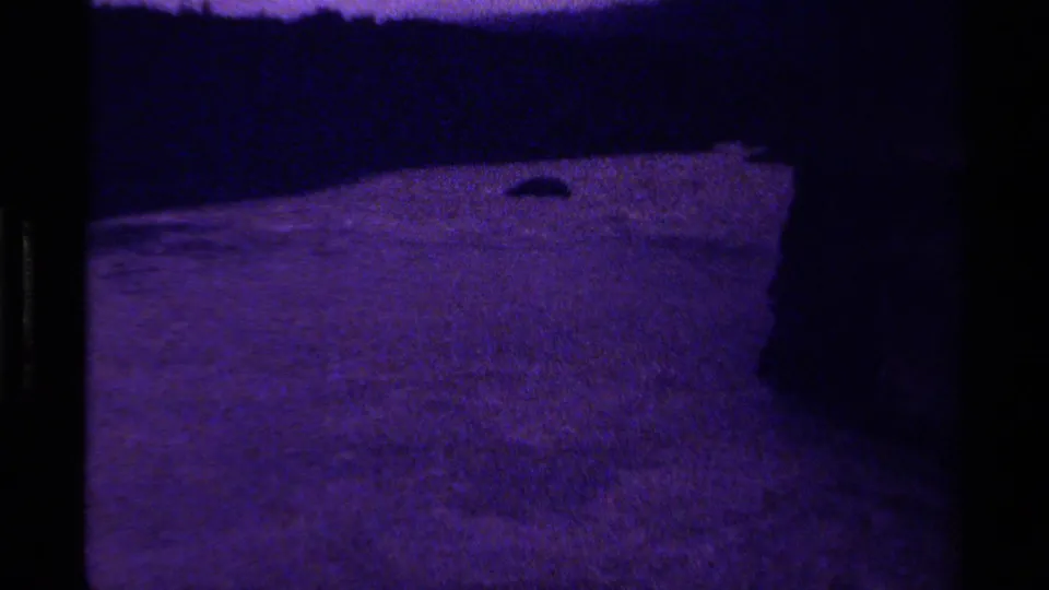 1979 Canadian 8mm frame of a dim, purple-tinted river bend, with rippled water moving beside a shadowed rock wall.