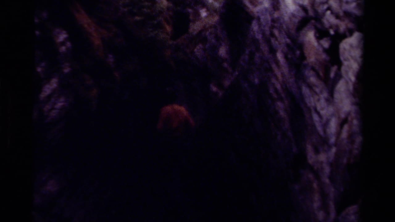 Dim 1979 Canada cave footage with a barely visible person moving near rough rock walls in deep shadow.