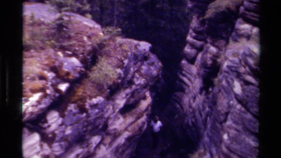 1979 Canadian 8mm home-movie frame showing a small figure moving near mossy stone walls in a shaded forest canyon.
