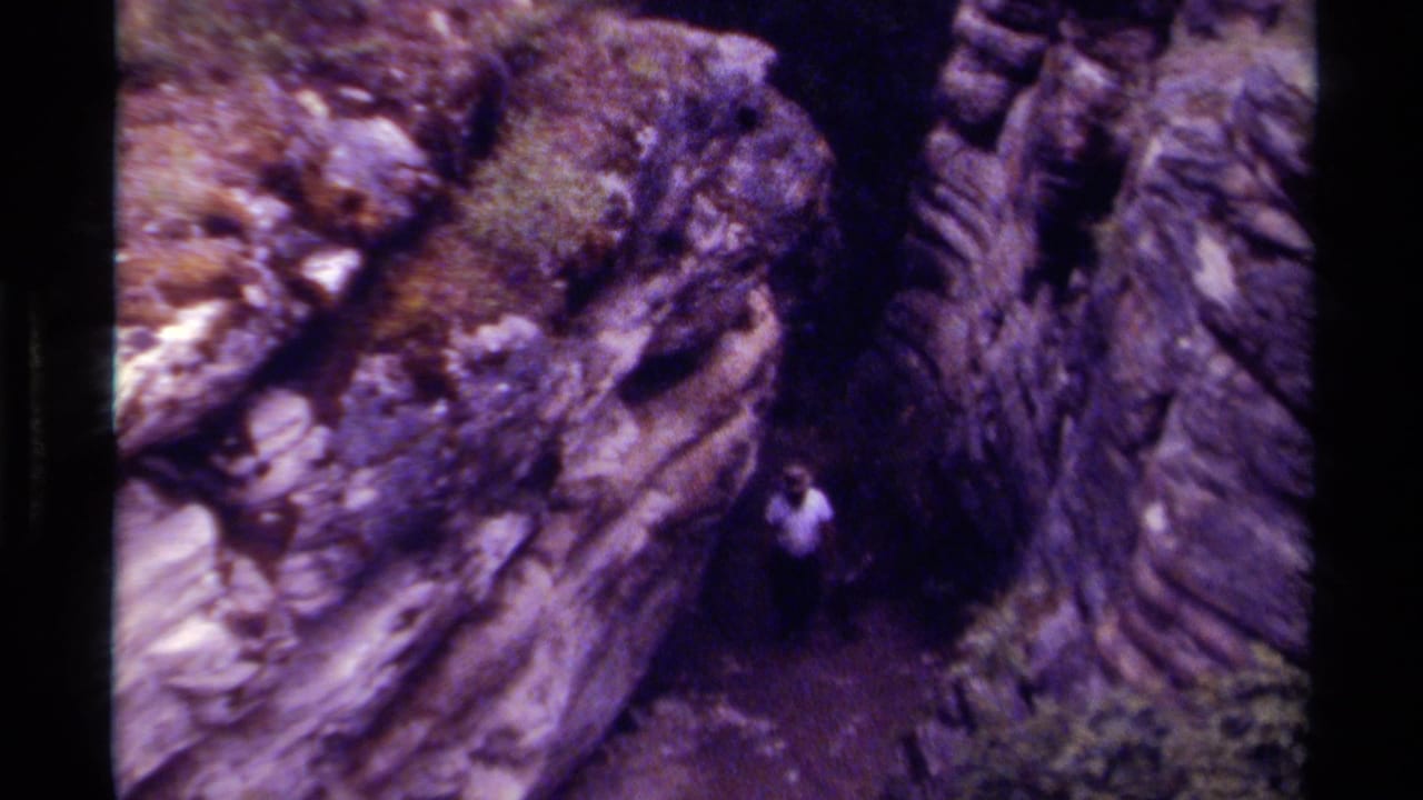 In 1979 Canada footage, a man in a light shirt appears small between layered rock walls in a narrow canyon passage.