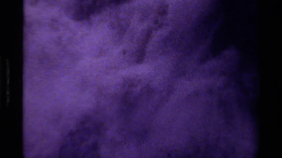 Grainy 1979 Canadian 8mm frame with purple swirling forms and indistinct dark patches.