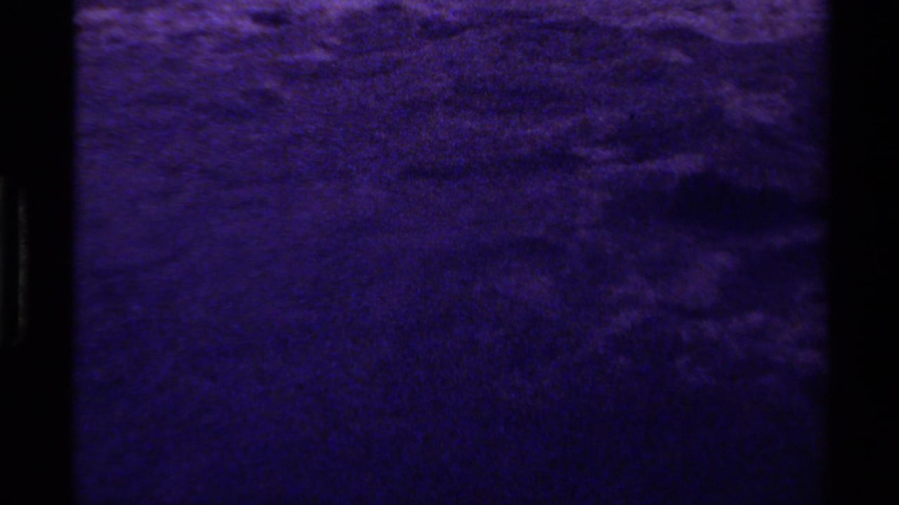 1979 Canadian 8mm frame of rippled water rendered in a deep purple cast, with visible grain and black gate border.