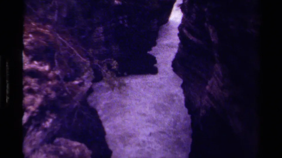 1979 Canada 8mm frame of a narrow mountain stream bordered by steep dark rock, with visible grain and color shift.
