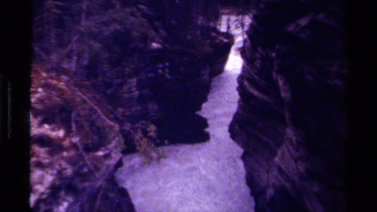 Canyon stream seen from above, bordered by dark rocks and dense vegetation.